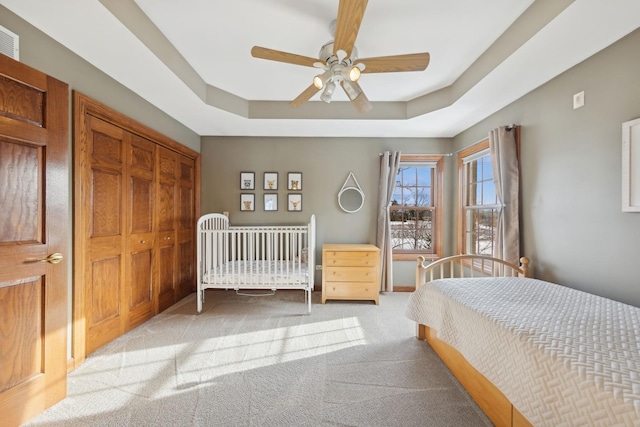 bedroom featuring light carpet, a closet, a raised ceiling, and a ceiling fan