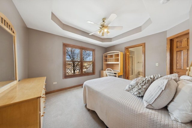 bedroom with a tray ceiling, light colored carpet, a ceiling fan, connected bathroom, and baseboards