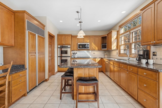 kitchen with stainless steel appliances, a center island, dark stone counters, and a sink