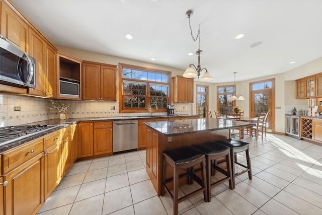 kitchen featuring a center island, decorative light fixtures, appliances with stainless steel finishes, dark stone counters, and a kitchen bar