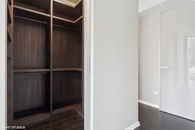 walk in closet with dark wood-style floors