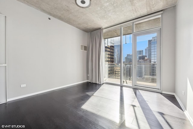 empty room with expansive windows, dark wood-type flooring, baseboards, and a city view