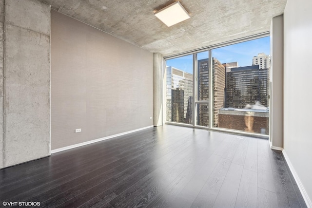 unfurnished room featuring a wall of windows, dark wood-style flooring, a city view, and baseboards