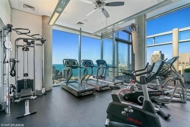 exercise room with ceiling fan, a view of city, visible vents, and a wall of windows