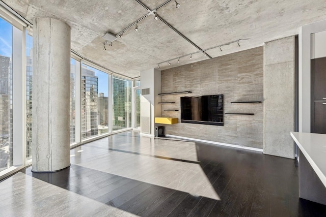 unfurnished living room with a view of city, rail lighting, expansive windows, and wood finished floors