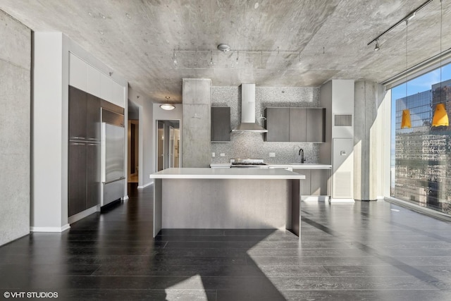 kitchen with wall chimney exhaust hood, modern cabinets, dark wood-type flooring, light countertops, and a sink