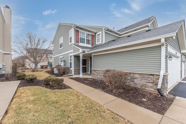 traditional-style house with a shingled roof, stone siding, an attached garage, and aphalt driveway