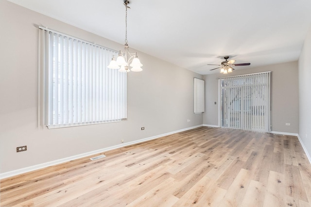 empty room with visible vents, a healthy amount of sunlight, wood finished floors, baseboards, and ceiling fan with notable chandelier