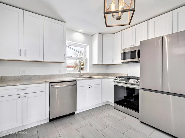 kitchen featuring light stone counters, stainless steel appliances, a sink, white cabinets, and pendant lighting