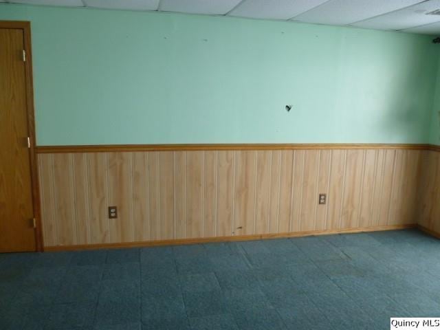 empty room featuring a paneled ceiling and wooden walls