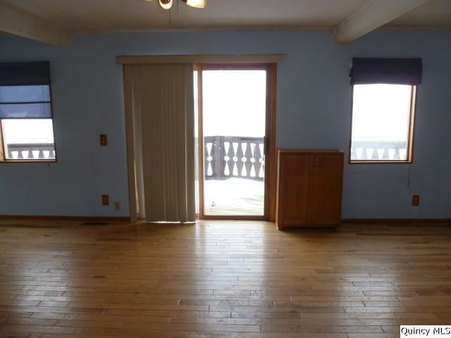 spare room featuring light wood-type flooring, a healthy amount of sunlight, and beam ceiling