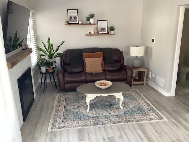 living room featuring light wood-style floors, a glass covered fireplace, visible vents, and baseboards