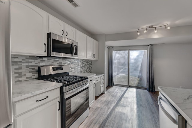 kitchen with appliances with stainless steel finishes, white cabinetry, light stone counters, and tasteful backsplash