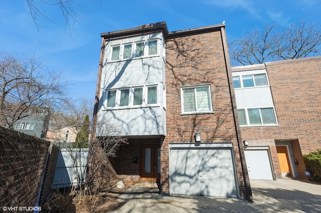 view of front of house featuring a garage, brick siding, decorative driveway, and fence