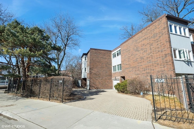 view of home's exterior with decorative driveway, brick siding, and fence