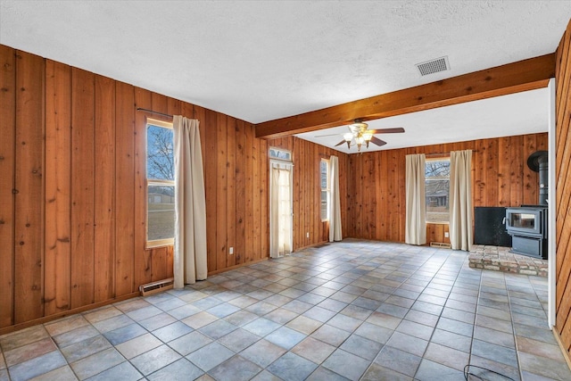 unfurnished living room featuring beam ceiling, a wood stove, visible vents, and a textured ceiling