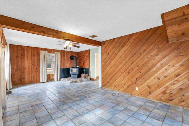 unfurnished living room featuring beamed ceiling, wooden walls, visible vents, and a wood stove