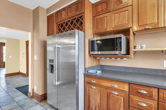 kitchen with brown cabinets, dark countertops, appliances with stainless steel finishes, light tile patterned flooring, and baseboards