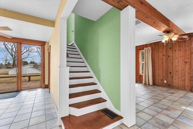 stairway with tile patterned flooring, visible vents, wooden walls, beamed ceiling, and a ceiling fan