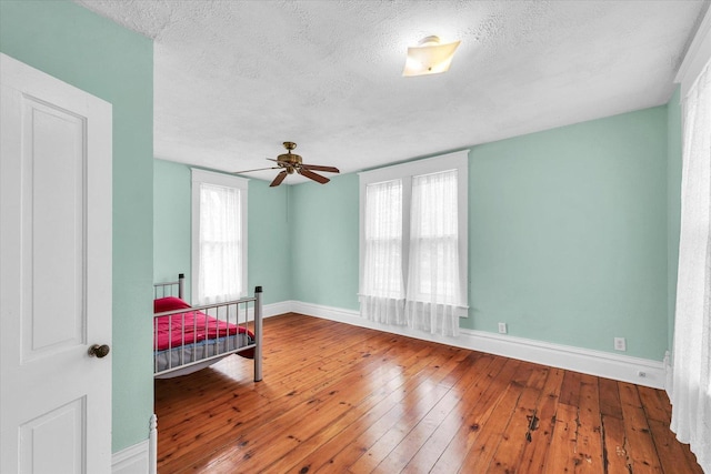 bedroom featuring multiple windows, a textured ceiling, baseboards, and hardwood / wood-style flooring