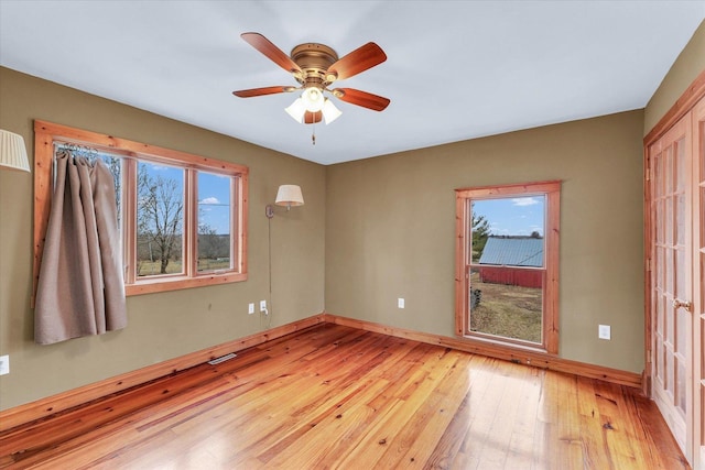 spare room featuring light wood-style flooring, a ceiling fan, and baseboards