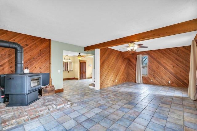 unfurnished living room featuring beamed ceiling, baseboards, wooden walls, and a wood stove