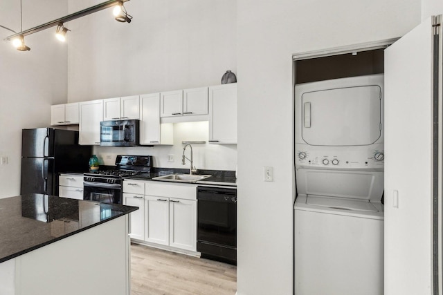 kitchen with stacked washer and dryer, a towering ceiling, black appliances, white cabinetry, and a sink