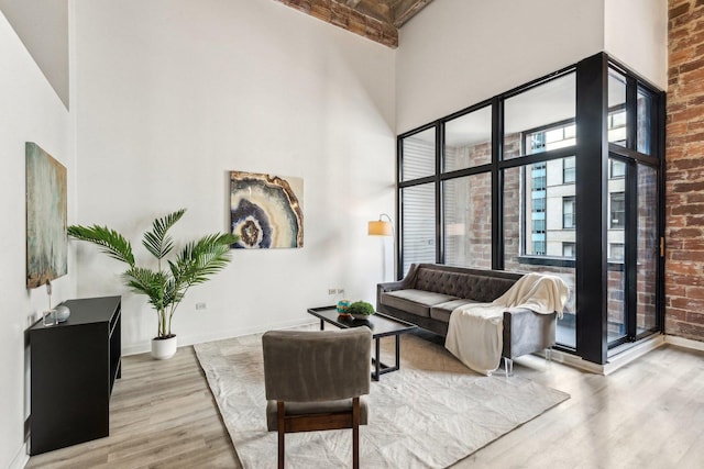 living room featuring a towering ceiling, light wood finished floors, and brick wall