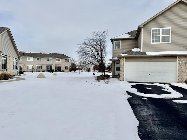 yard layered in snow featuring aphalt driveway and an attached garage