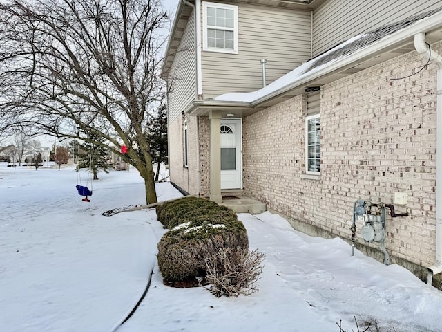 snow covered property entrance featuring brick siding