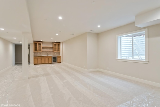 unfurnished living room with wine cooler, recessed lighting, light colored carpet, a sink, and baseboards