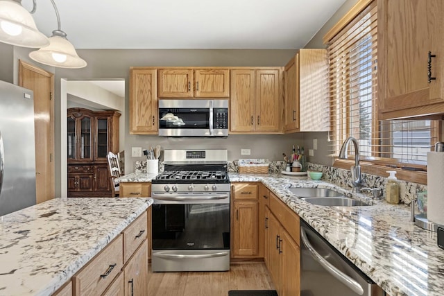 kitchen featuring hanging light fixtures, light wood-type flooring, stainless steel appliances, light stone countertops, and sink