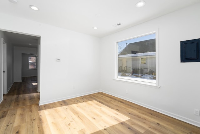 empty room with recessed lighting, electric panel, light wood-style flooring, and baseboards