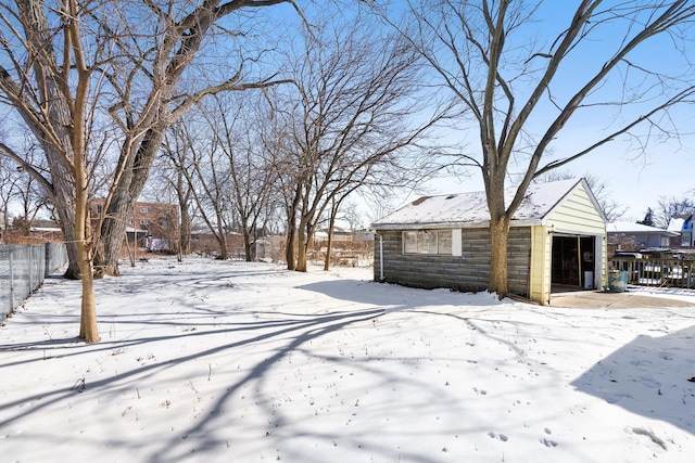 yard layered in snow with a garage, an outbuilding, and fence