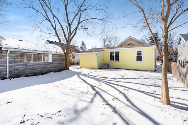 snow covered rear of property featuring central AC unit and fence