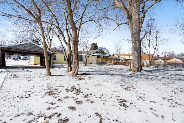 snow covered back of property with a carport, a residential view, and fence