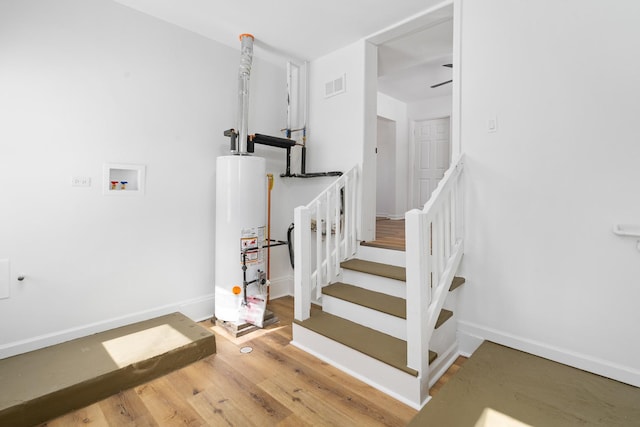 stairway featuring gas water heater, visible vents, baseboards, and wood finished floors