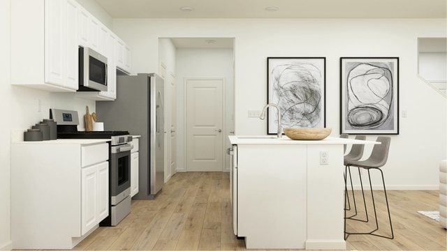 kitchen with appliances with stainless steel finishes, a breakfast bar, sink, white cabinetry, and light hardwood / wood-style floors