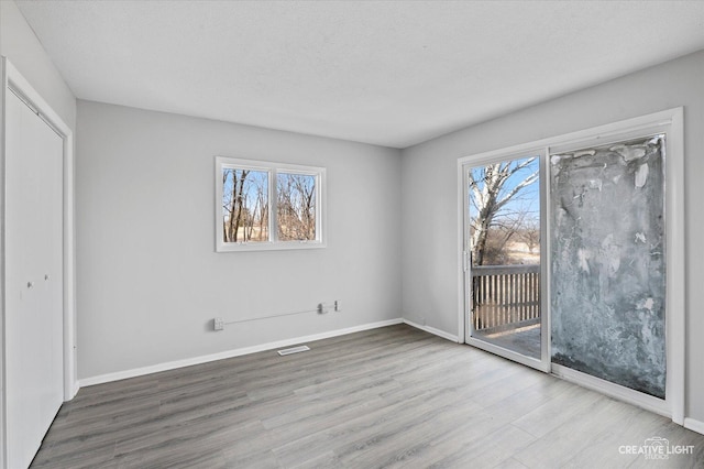 unfurnished bedroom featuring multiple windows, hardwood / wood-style floors, access to outside, and a textured ceiling