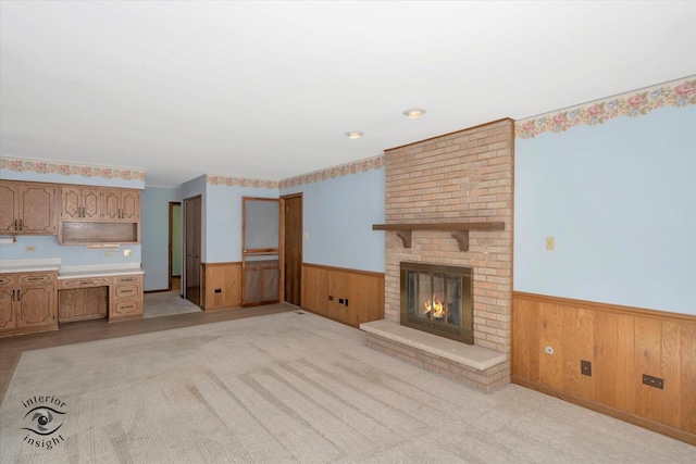 unfurnished living room with a brick fireplace, wood walls, wainscoting, and light colored carpet