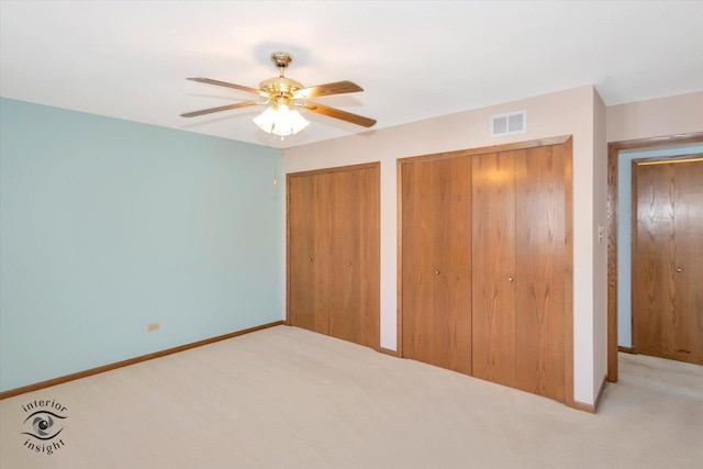 unfurnished bedroom featuring light colored carpet, visible vents, baseboards, and two closets