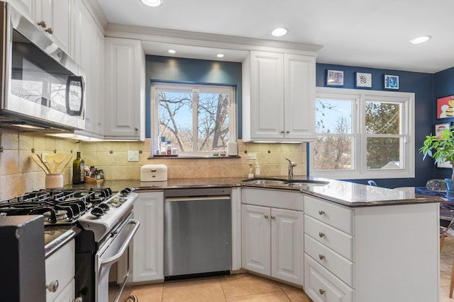 kitchen featuring dark stone countertops, appliances with stainless steel finishes, a peninsula, white cabinets, and a sink