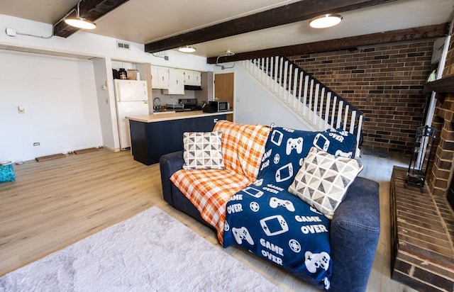 living area featuring visible vents, brick wall, light wood-style flooring, stairway, and beamed ceiling