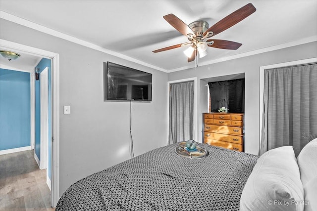 bedroom featuring crown molding, multiple closets, ceiling fan, wood finished floors, and baseboards