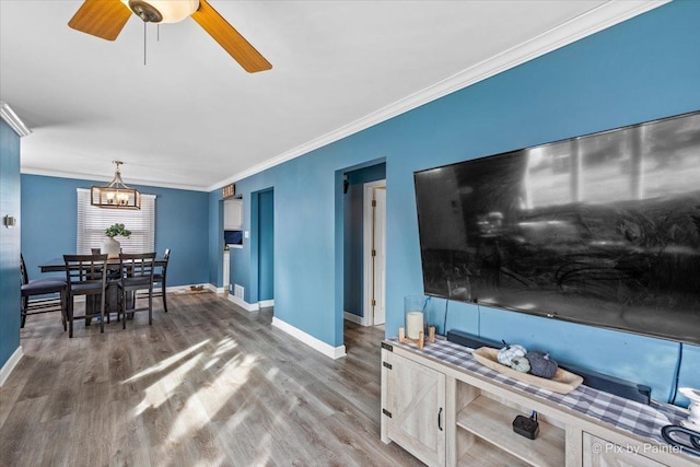 interior space with ornamental molding, ceiling fan with notable chandelier, baseboards, and wood finished floors