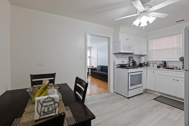 kitchen with white appliances, light wood-style flooring, visible vents, and white cabinetry