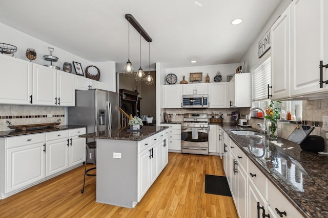 kitchen featuring appliances with stainless steel finishes, decorative light fixtures, a center island, sink, and white cabinetry