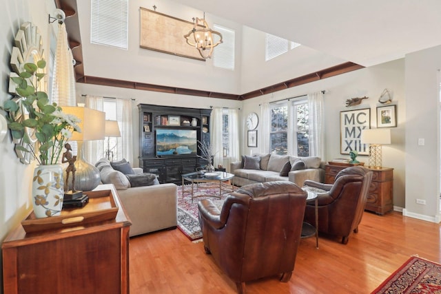 living room with baseboards, a notable chandelier, light wood-style flooring, and a high ceiling