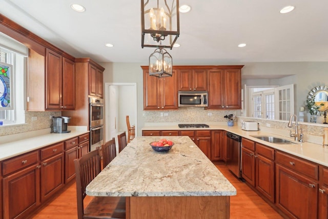 kitchen with decorative light fixtures, stainless steel appliances, light wood-style flooring, a sink, and a kitchen island