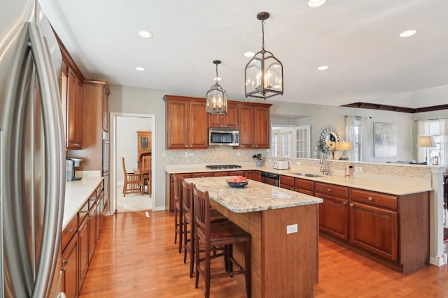 kitchen featuring appliances with stainless steel finishes, light wood-style floors, a kitchen island, a peninsula, and a kitchen bar